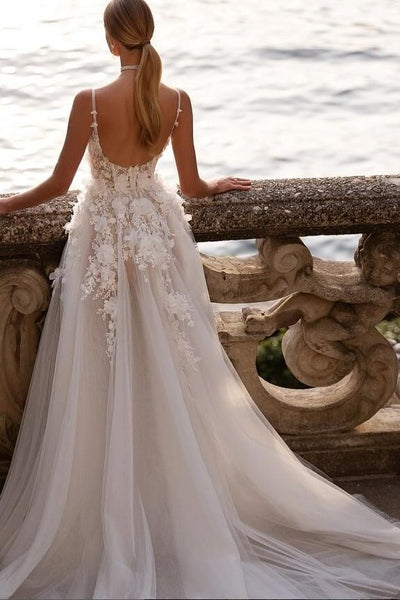 Woman in a white wedding dress with floral details standing by a stone railing.