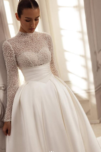 Woman wearing a beaded long-sleeve wedding dress in a softly lit room.