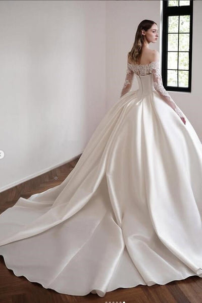 Woman wearing a white wedding dress with lace sleeves in a room with a window.