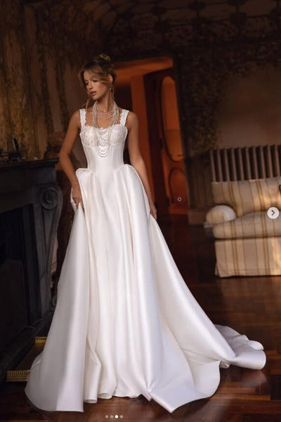 Woman in a white wedding dress standing in a room with wooden floor and furniture.